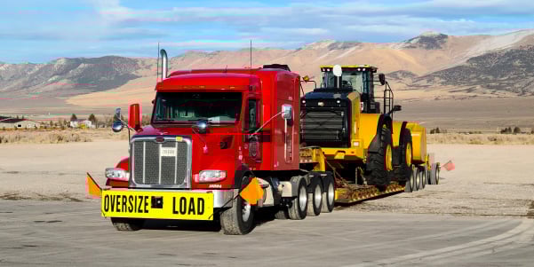 A red ATS tractor carrying an OD load of construction equipment.