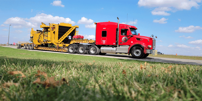 Bright red ATS truck hauling yellow construction equipment. The sky is bright with a few clouds.