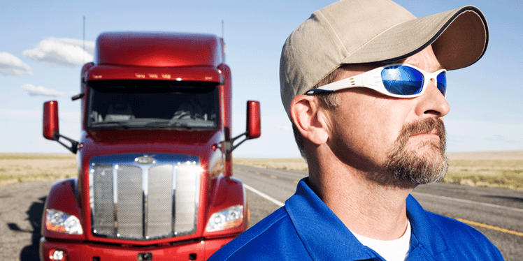 Man in blue standing in front of his red truck on the side of the highway, tips for hauling military freight, DOD, secure, ATS, Anderson Trucking Service