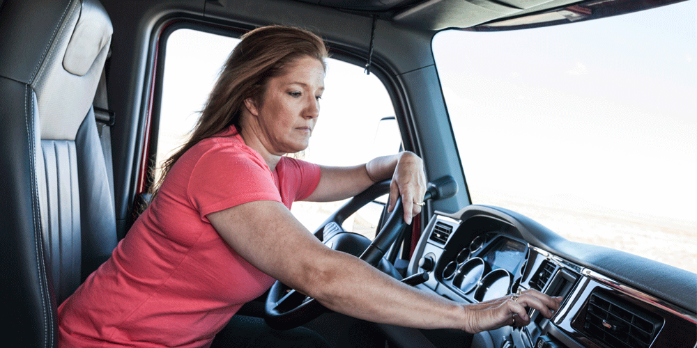 Woman driver parked and using the GPS mapping device in the cab of a commercial truck.