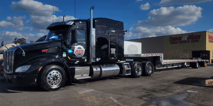 Shiny black truck with step-deck trailer.