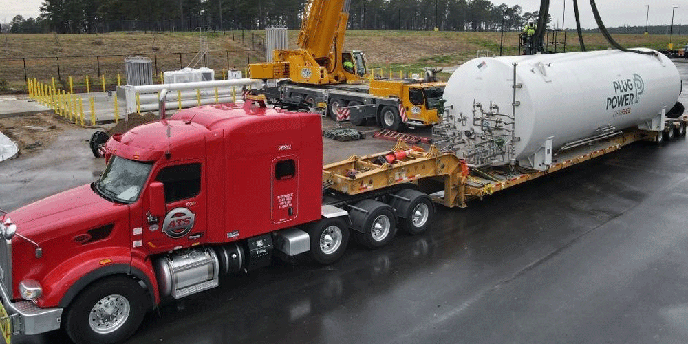 Red ATS semi-truck getting loaded at a shipper. A crane is placing a large tank on the specialized trailer.
