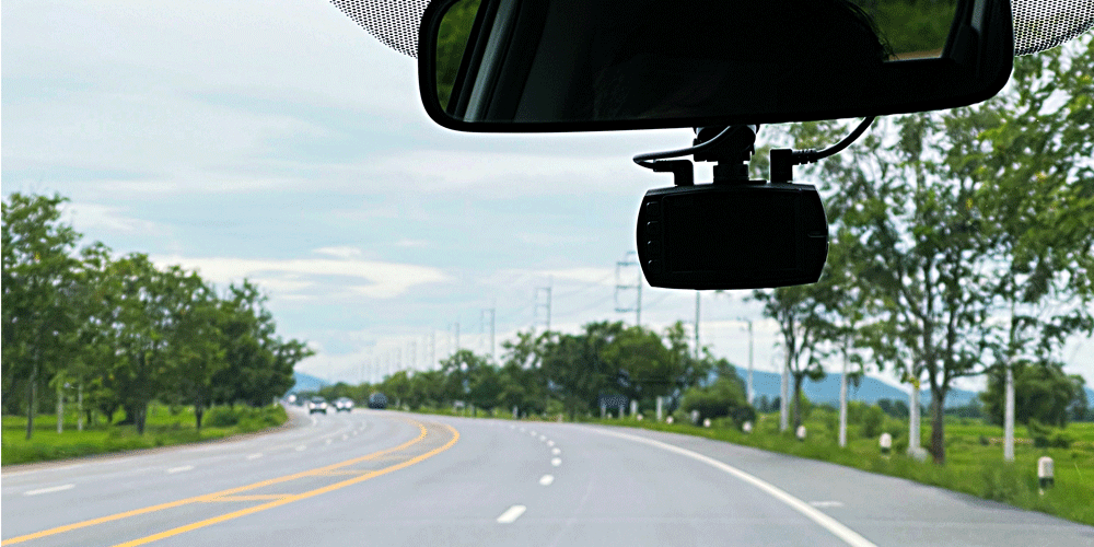 View out the windshield. The rearview mirror and a dash cam can be seen.