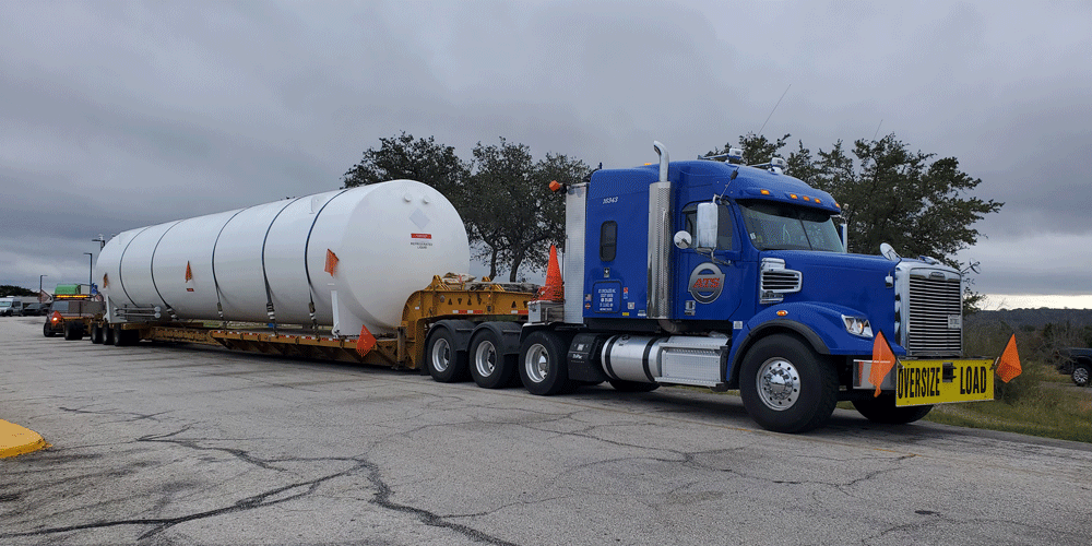 Blue semi-truck with large white cylinder being hauled on the yellow trailer.
