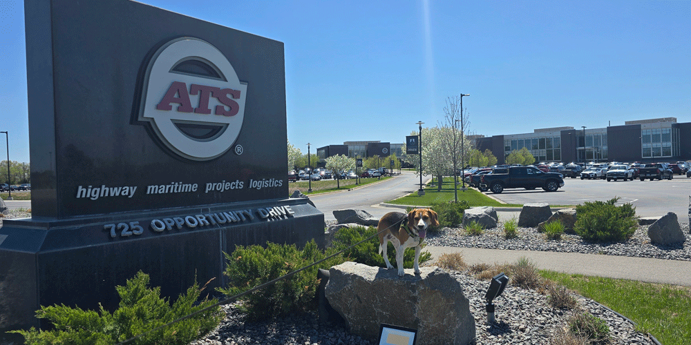 Granite ATS sign in front of a parking lot and building. A dog smiles in front of the sign on a boulder.