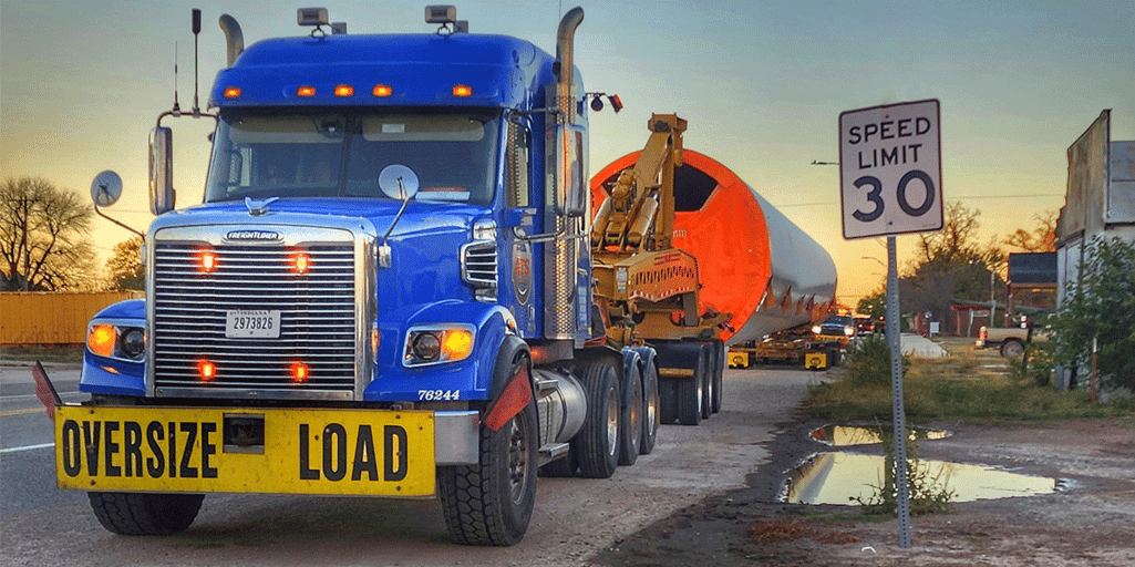 A blue ATS truck hauling an oversized load down a local road.