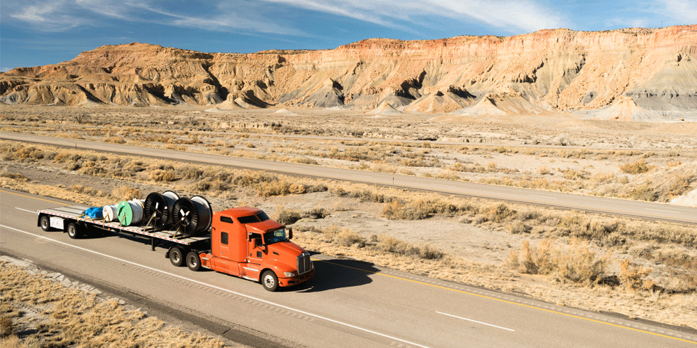 Orange semi-truck hauling multiple coils through the desert. 