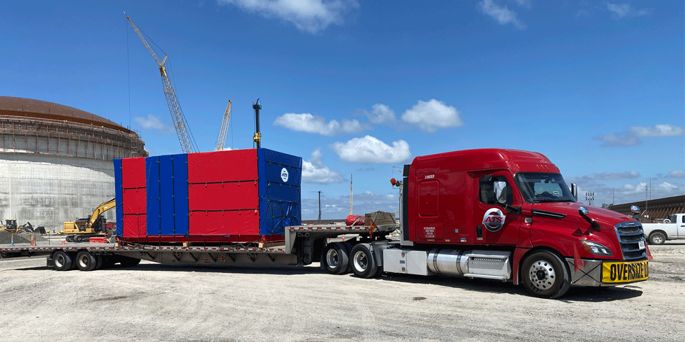 Red semi-truck with red and blue tarped squarish load.