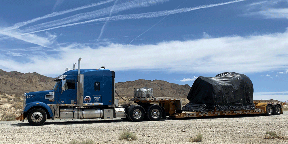Semi-truck with tarped flatbed load.