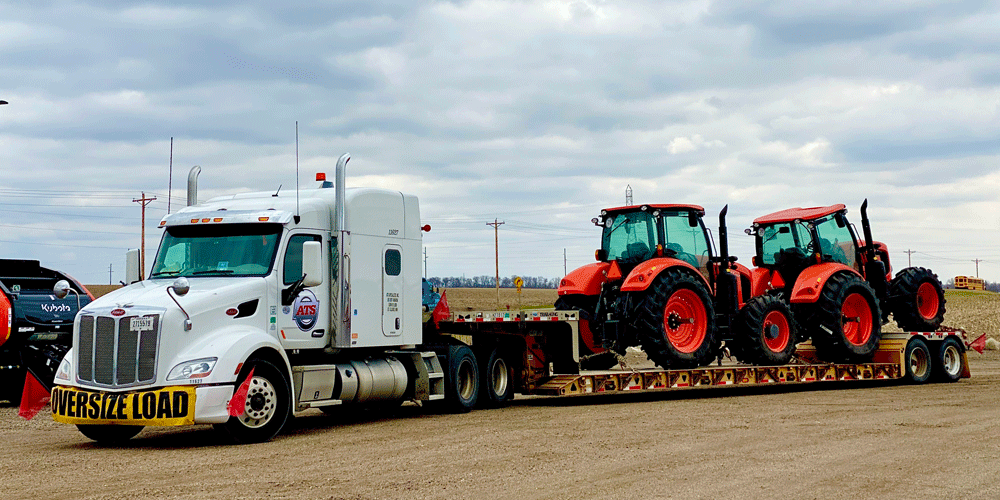 Over-dimensional load hauling two red tractors.