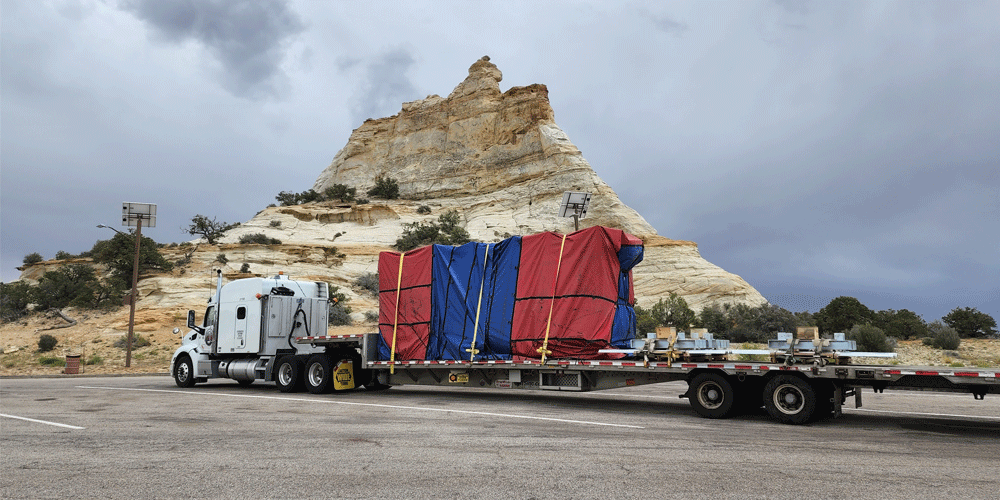 Tarped flatbed load parked in front of a white rock formation.