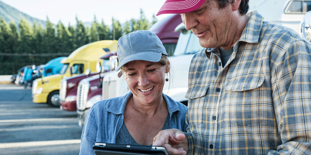 Married Team Drivers Reading Tablet outside in truck yard.