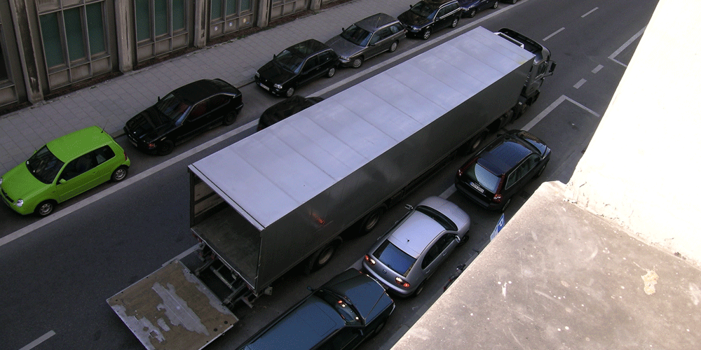A bird's eye view of a semi unloading freight in the middle of a busy street.