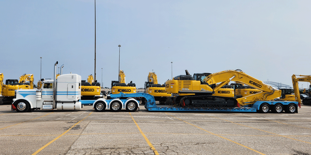 White semi-truck hauling yellow construction equipment.