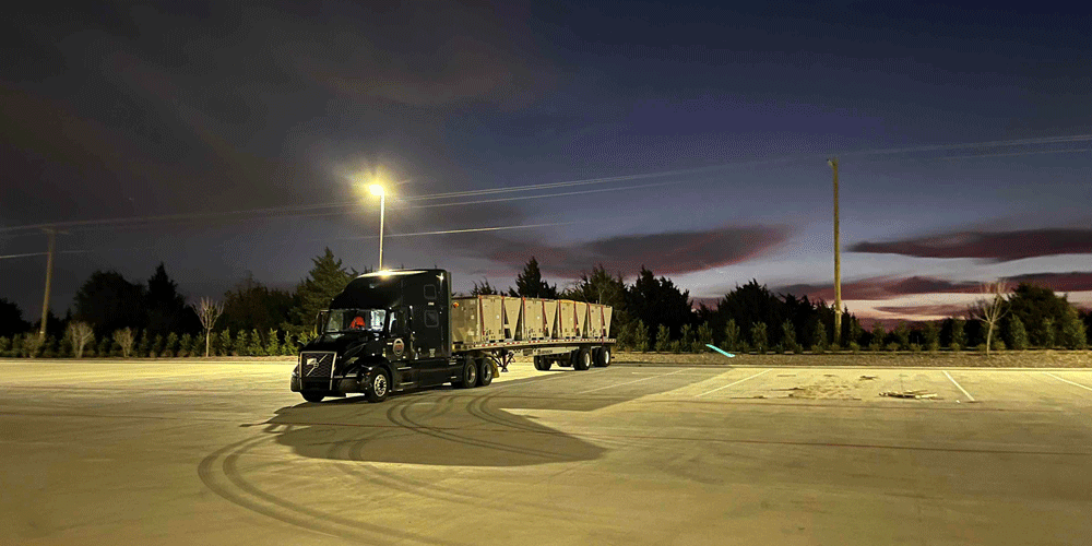 Black tractor parked in the middle of an empty parking lot. The sun is rising in the background.