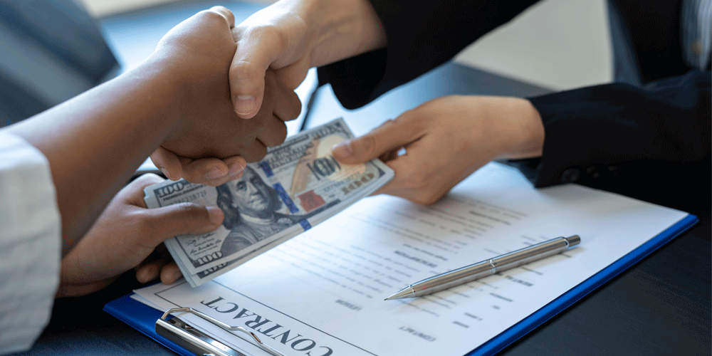 Two people shaking hands and exchanging money.