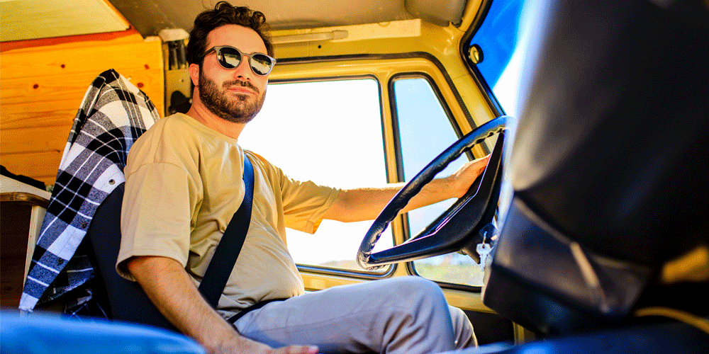 Young bearded truck driver in sunglasses inside the cab of his truck.