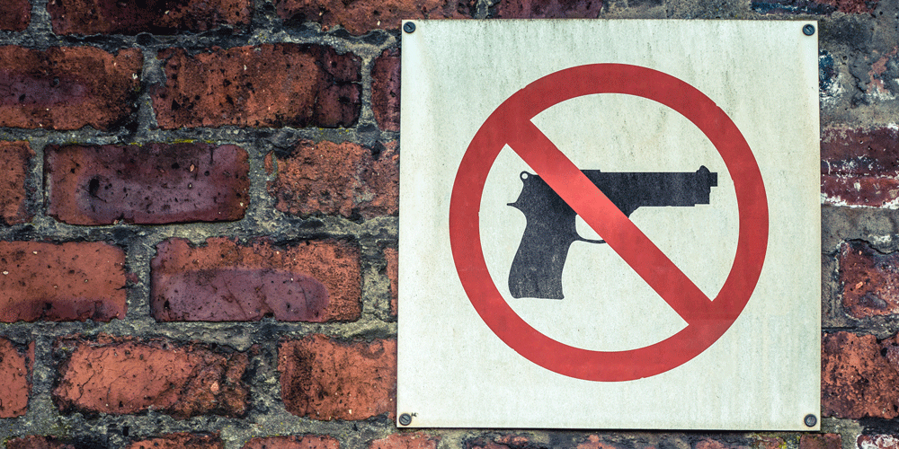 A sign with a crossed out gun on it hanging on a red brick wall.
