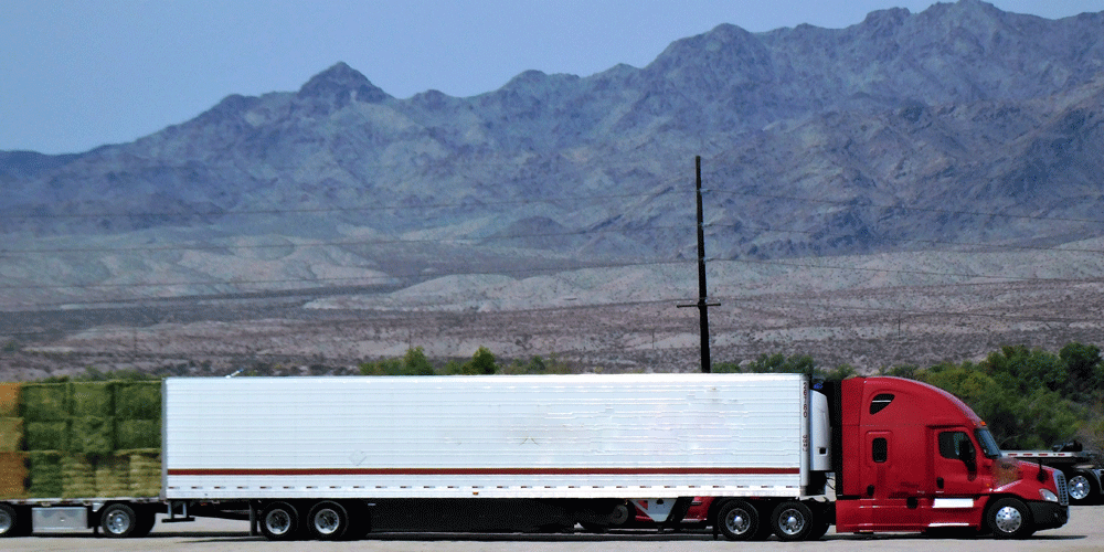 Red tractor and dry van trailer parked in front of mountains.