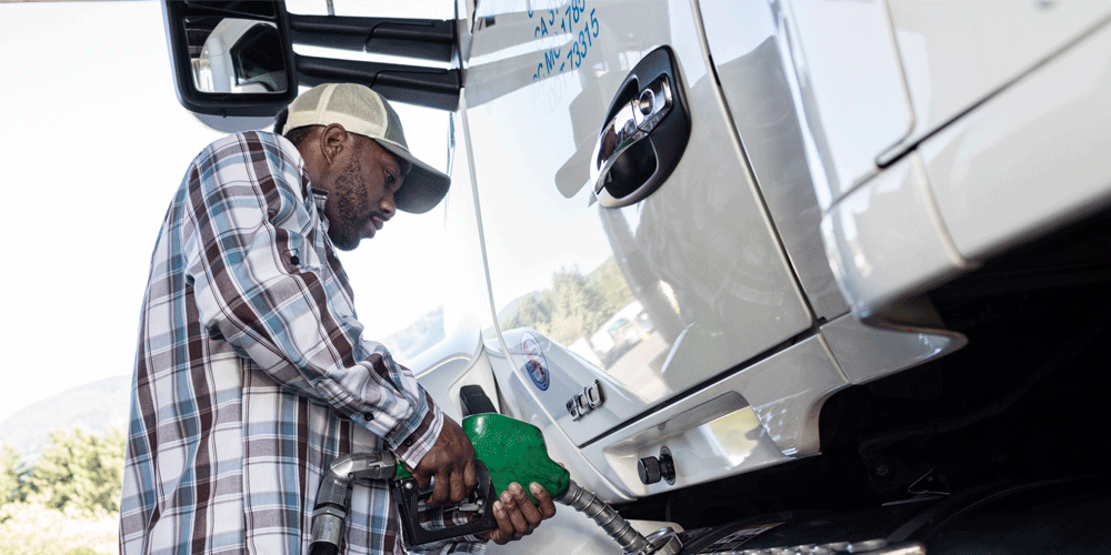 Man in flannel button-down and hat fueling his white semi-truck.