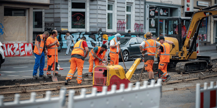 Construction workers working on a city road. The buildings in the background are full of graffiti.