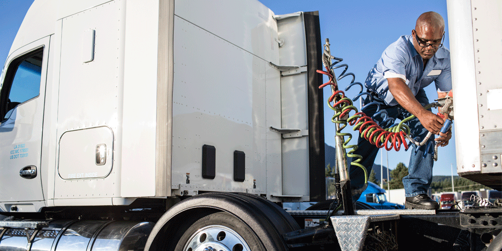 Man attaching cables on semi-truck trailer.