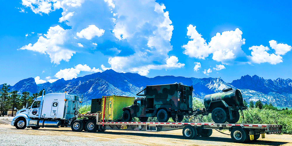 Military vehicles being hauled on a stepdeck trailer.