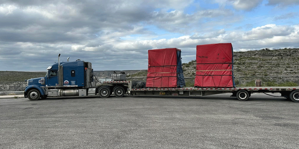 Transporting a tarped and secured load on a flatbed trailer through a mountainous region.