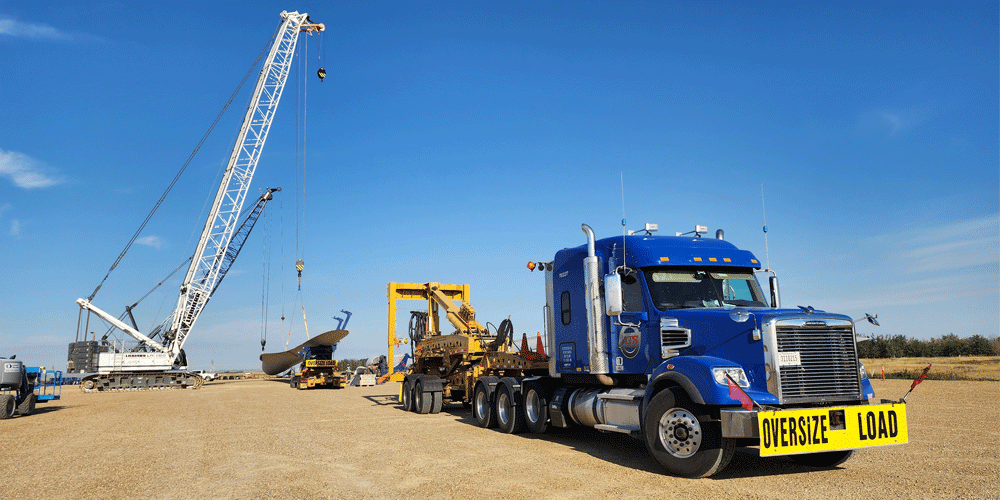 Blue semi-truck with a crane loading freight in the background.