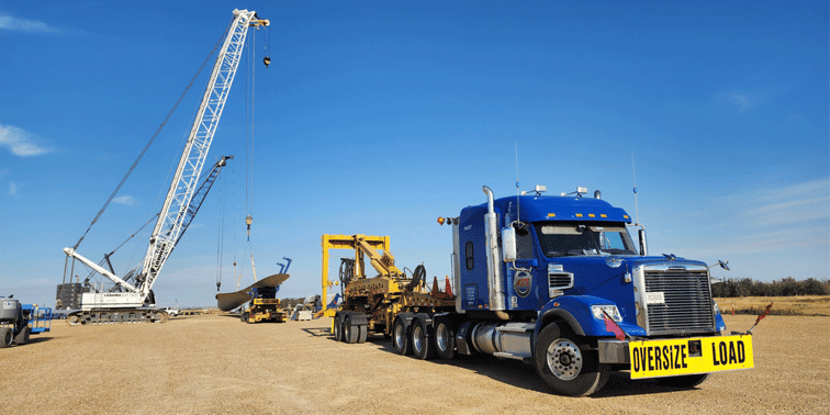Blue semi-truck with a crane loading freight in the background.