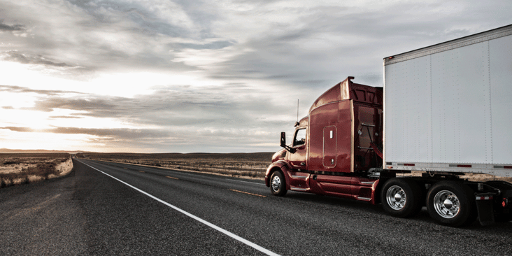 Side view of red tractor and van trailer driving down the highway during golden hour.
