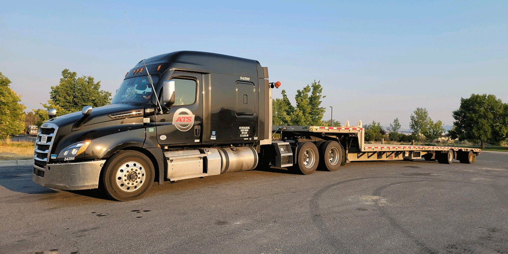 Black semi-truck with attached empty step-deck trailer.