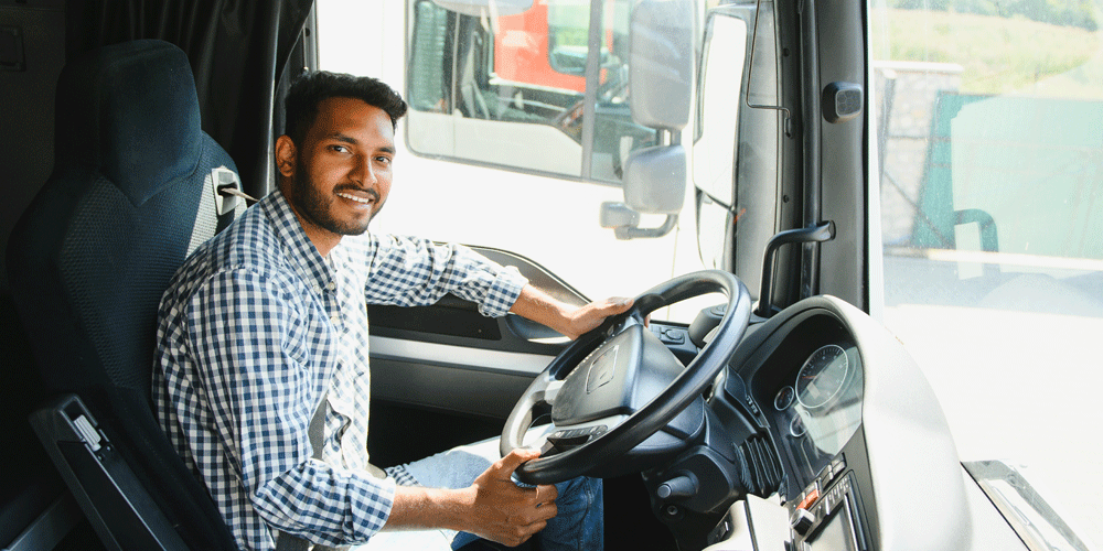 Smiling truck driver behind the wheel of his rig. He smiles and wears a checkered button-down.