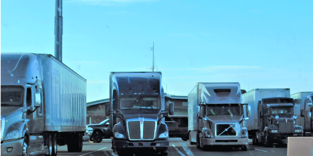 Trucks in a line parked in front of a truck stop. 