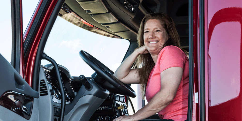 Portrait of a female truck driver sitting behind the wheel of her red rig.