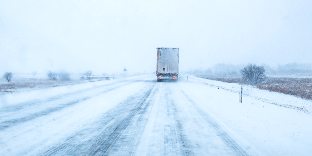 The back of a snowy semi-truck on a snow covered road.