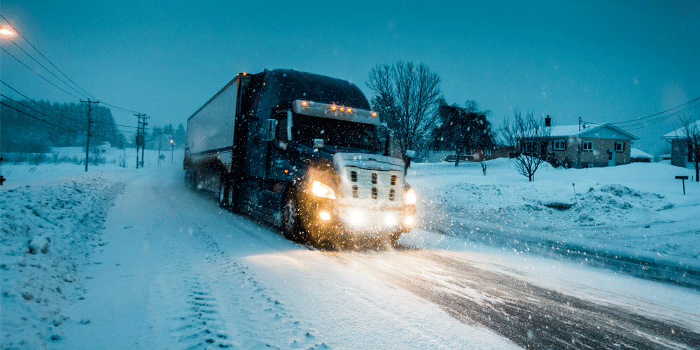 Semi-truck driving in a blizzard on a back road near homes.