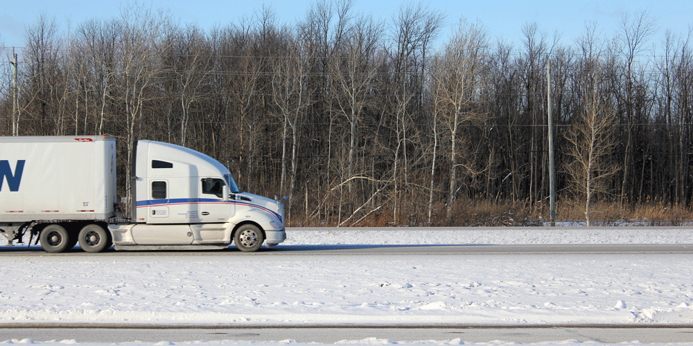 Semi-truck with van trailer driving on a rural snow-covered road.
