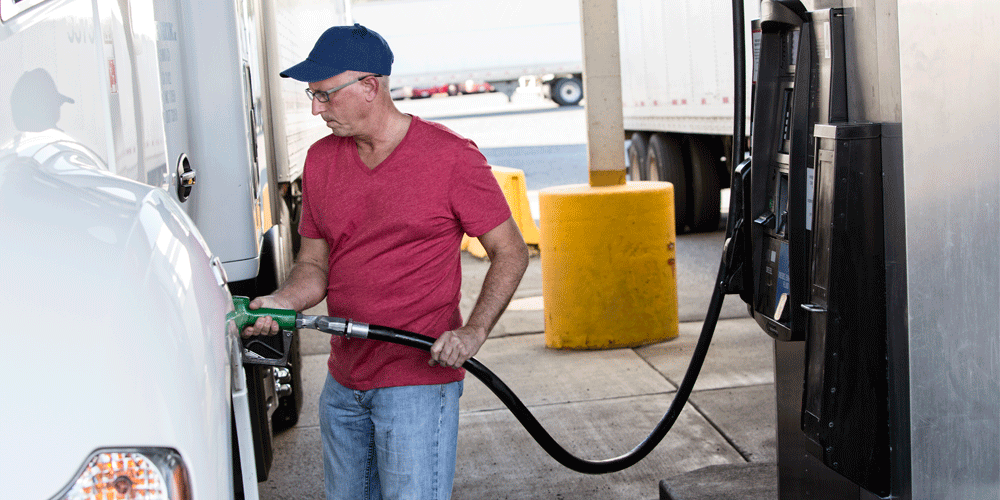 Man in red shirt and blue hat fueling his white semi-truck.