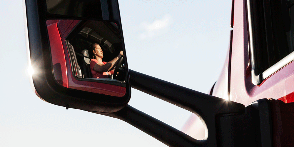 Female truck driver shown in side mirror.