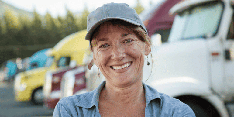 Woman truck driver smiles in front of a fleet of semi trucks