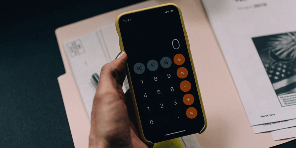 Holding an iPhone calculator above a folder of paperwork.