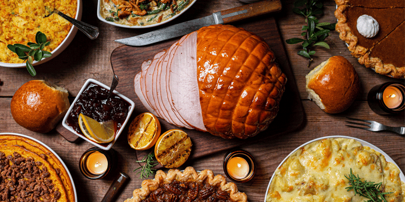 A festive, holiday feast of ham, pie, green beans, potatoes, and macaroni spread across a table