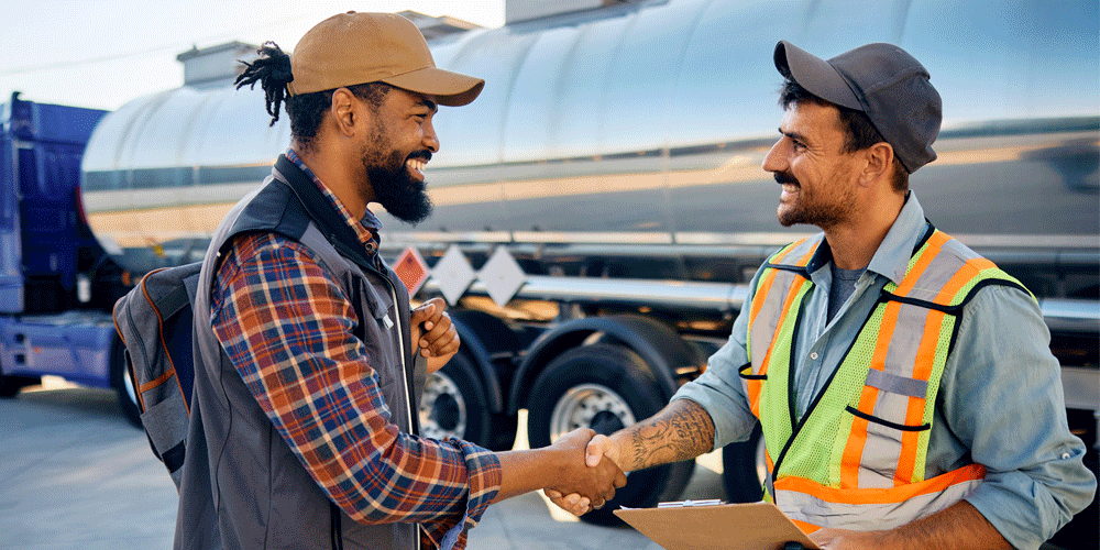 Two drivers shaking hands in front of a tanker trailer.