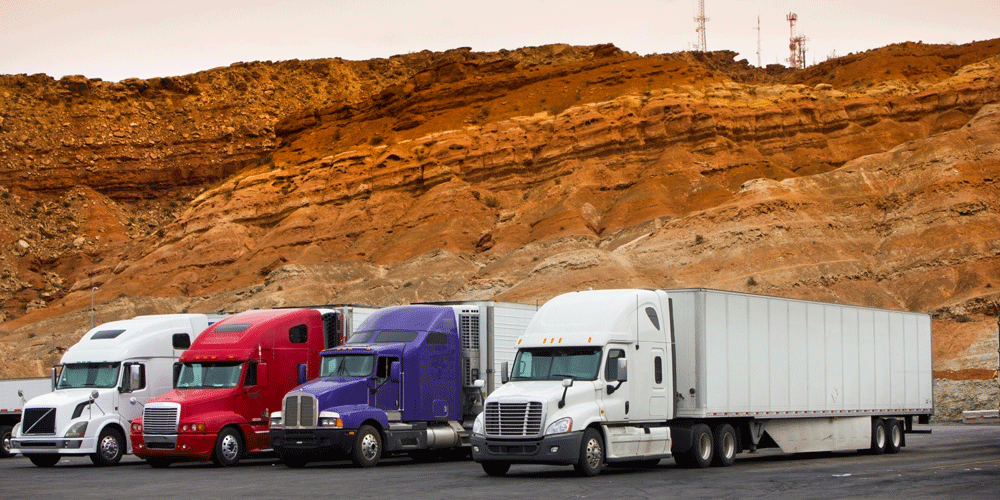 Four van trucks lined up on the road in front of orange-colored rock formations.