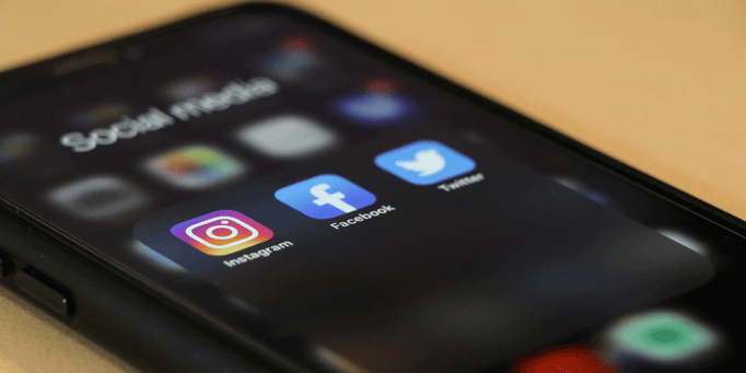A phone with the Instagram, Facebook, and Twitter icons shown.
