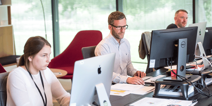 Three office workers sitting behind computer screens at one long desk, how to research trucking companies