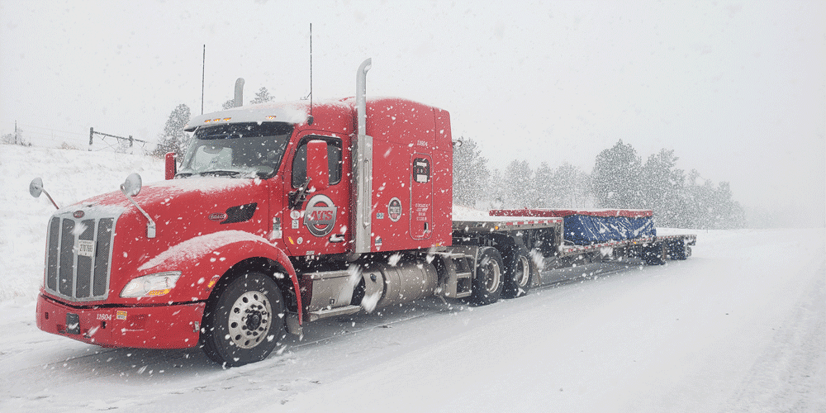 ATS flatbed truck with a tarped load on a snowy road