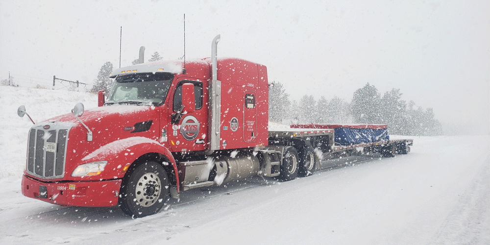 A red semi-truck hauling a flatbed stepdeck trailer with a tarped load.