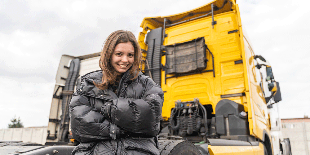 Young female truck driver smiling as she sits on the back of her semi-truck.